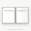 An open tabbed monthly calendar planner shown from above on a light gray background. The pages are white with gray grid lines and headers, bound by a gold spiral in the center.