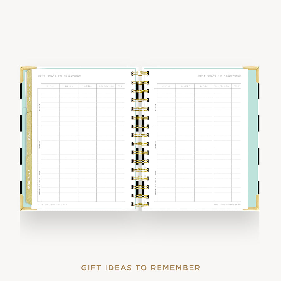 An open spiral-bound planner or notebook showing two white pages with grid tables and the heading 'GIFT IDEAS TO REMEMBER.' The cover edges are pale mint green and gold, with black side tabs.