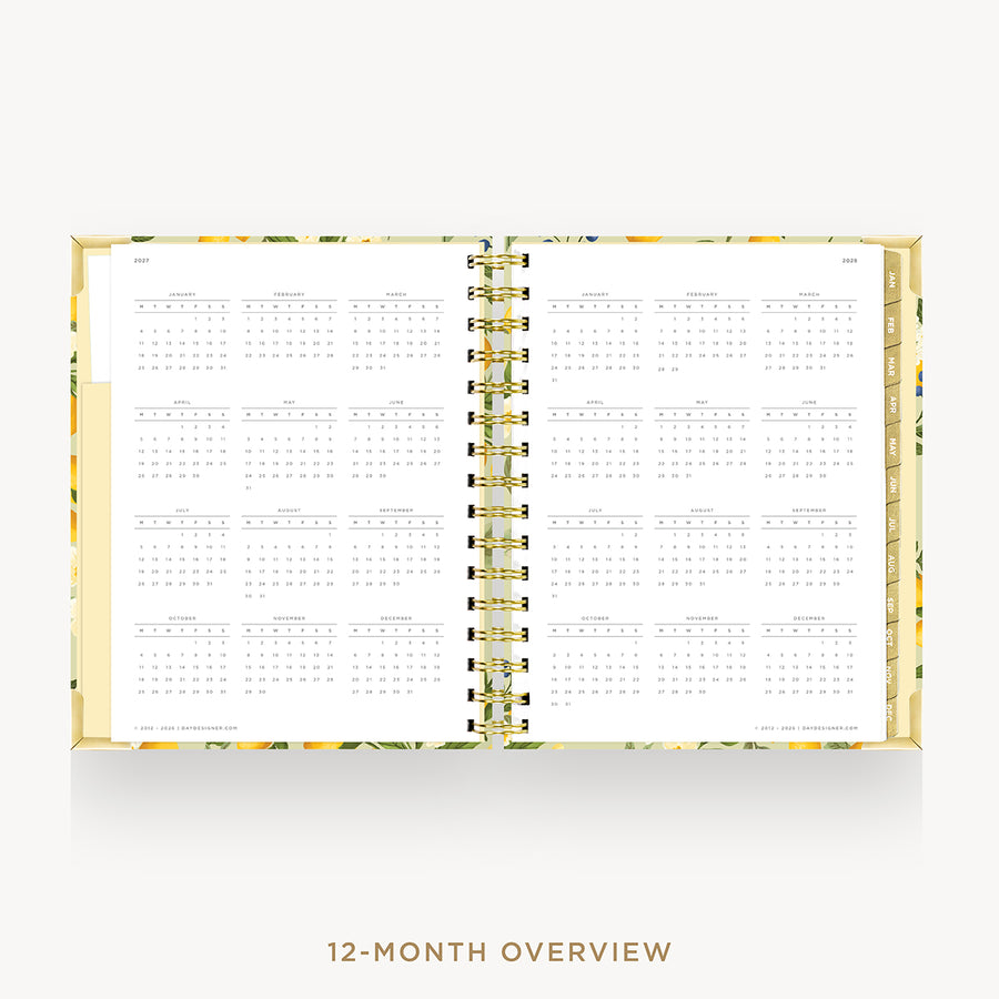 An open 12-month overview planner with a gold spiral binding and a yellow floral patterned cover, displayed on a light gray background with the text '12-MONTH OVERVIEW' below.