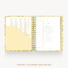 An open Day Designer pocket planner with a floral-patterned cover, gold spiral binding, a pocket, sticky notes, and a ruler, shown on a light gray background with the text 'POCKET, STICKERS AND RULER' below.