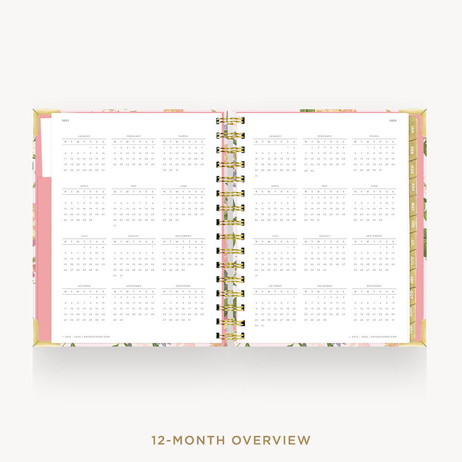 An open 12-month spiral planner or calendar with white pages showing monthly grids, a pink cover edge, and a floral-patterned cover, photographed on a light gray background with the text '12-MONTH OVERVIEW' below.
