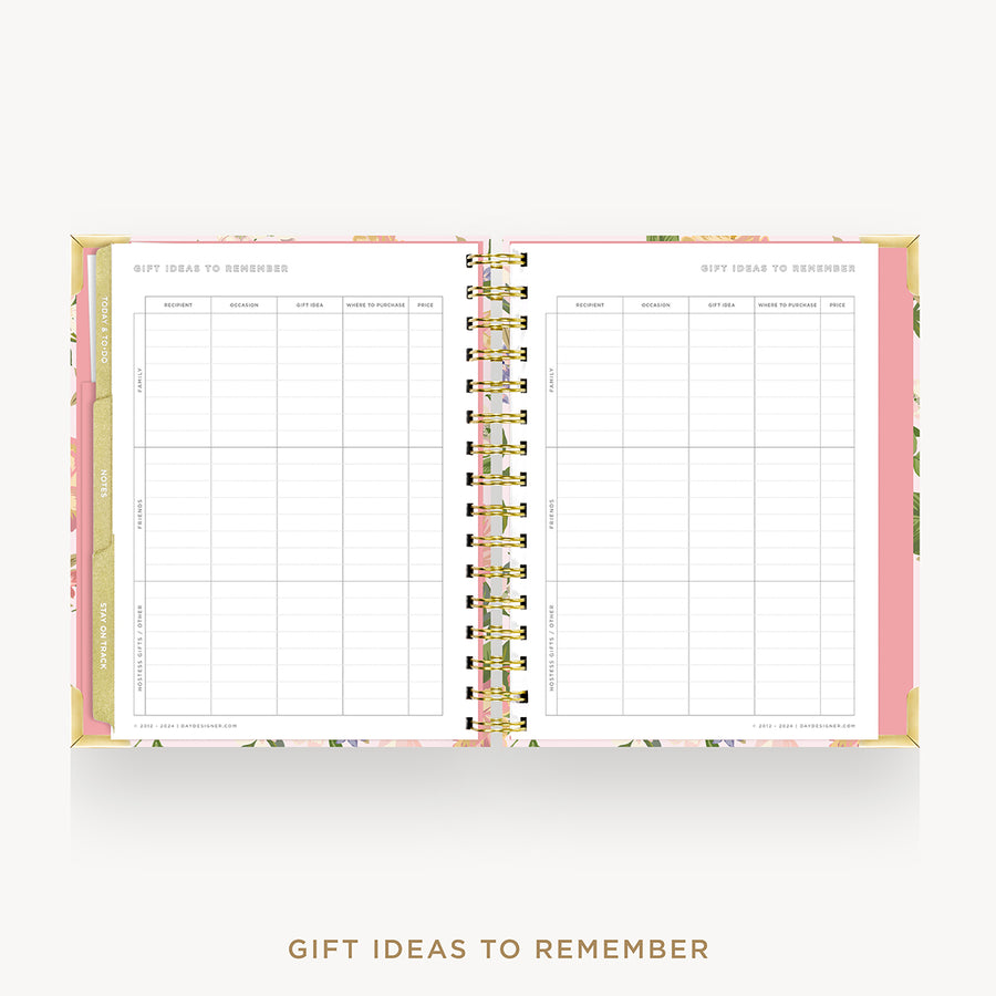 An open spiral-bound planner or notebook with floral-patterned pink and gold covers, showing two printed tables titled 'GIFT IDEAS TO REMEMBER' on the inner pages, set against a light gray background with matching text below.