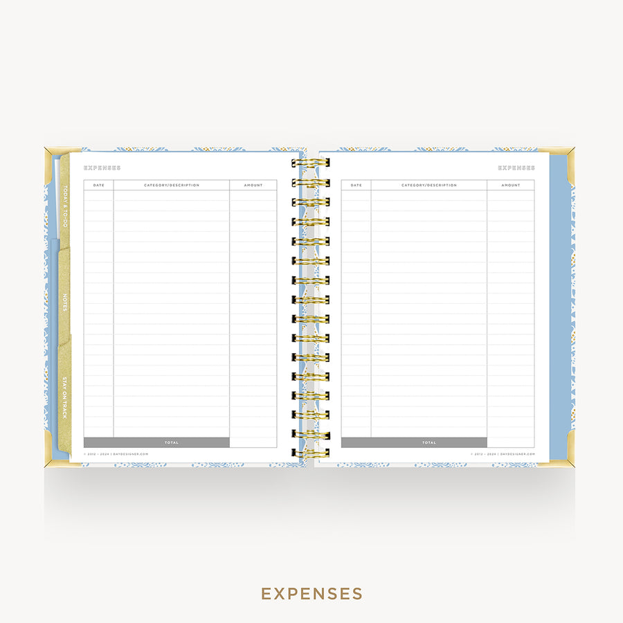 An open spiral-bound planner showing the expenses page with lined columns, a gold wire binding, and a light blue patterned cover, centered on a light gray background with the word EXPENSES below.