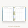 An open spiral-bound gift tracker planner on a light gray background. The pages are white with light blue borders and gold accents, featuring tables for recording gift ideas.