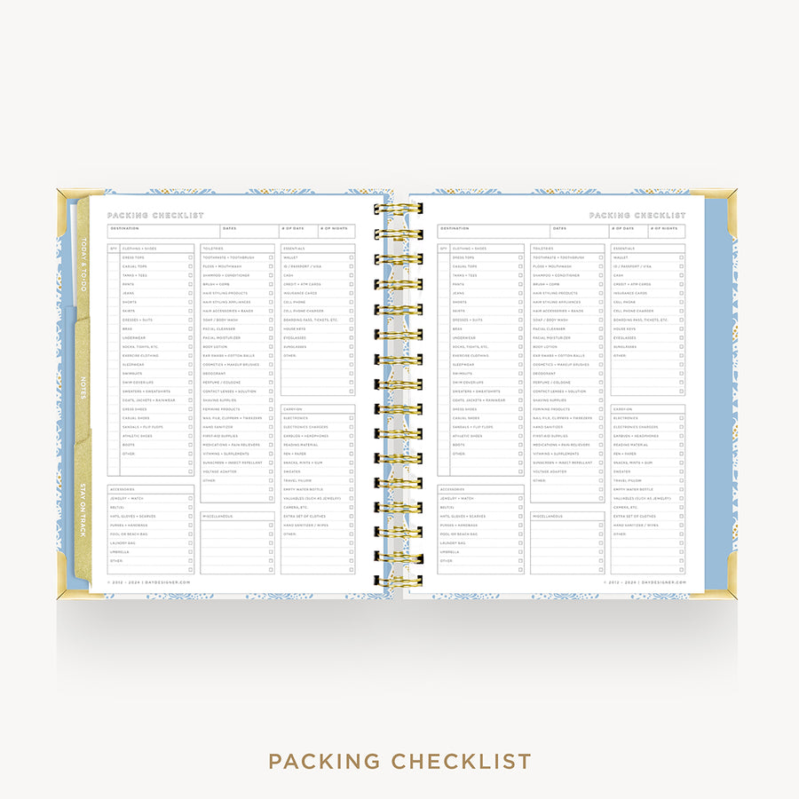 An open spiral-bound planner or notebook showing a packing checklist page spread across both sides, with a gold spiral binding and a light blue patterned cover, on a light gray background with the text 'PACKING CHECKLIST' below.