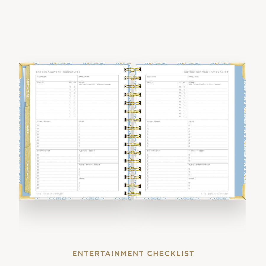 An open spiral-bound planner or notebook showing two printed checklist pages titled 'ENTERTAINMENT CHECKLIST.' The pages are white with gray lines and tables, bordered by a pale blue patterned cover and gold-toned spiral binding.