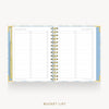 An open spiral-bound bucket list planner on a light gray background. The pages are lined with check boxes and labeled 'BUCKET LIST' items, with a gold spiral binding and a light blue and white patterned cover.
