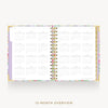 An open 12-month overview planner with a white interior page layout, a pastel floral patterned cover, and gold-toned spiral binding, shown on a light gray background with the text '12-MONTH OVERVIEW' below.