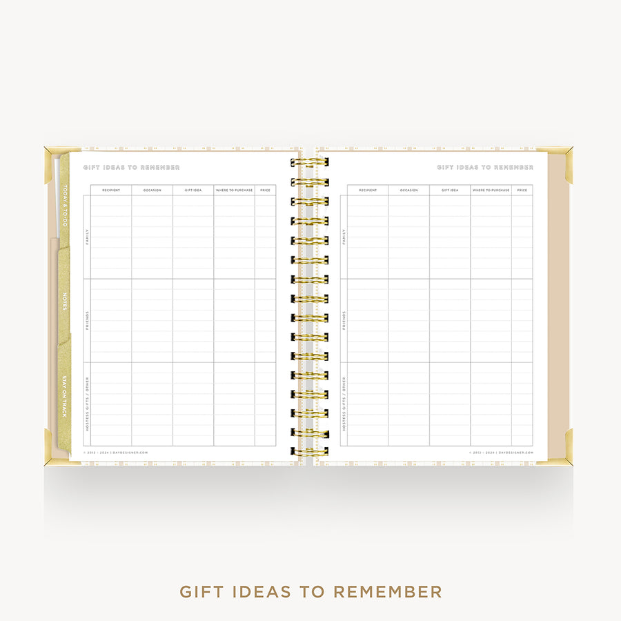 An open spiral-bound planner or notebook with gold-toned binding and white pages, showing a gift ideas to remember tracking table on the left and a blank page on the right, centered on a light gray background with the text 'GIFT IDEAS TO REMEMBER' below.