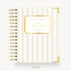 A Day Designer spiral notebook with a cream and gold striped cover, featuring a gold-bordered label in the center and gold wire binding on the left, shown on a light gray background.