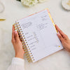 Person holding a planner with handwritten notes on a light surface