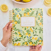 Hand holding a notebook with lemon design on a white surface with lemons around