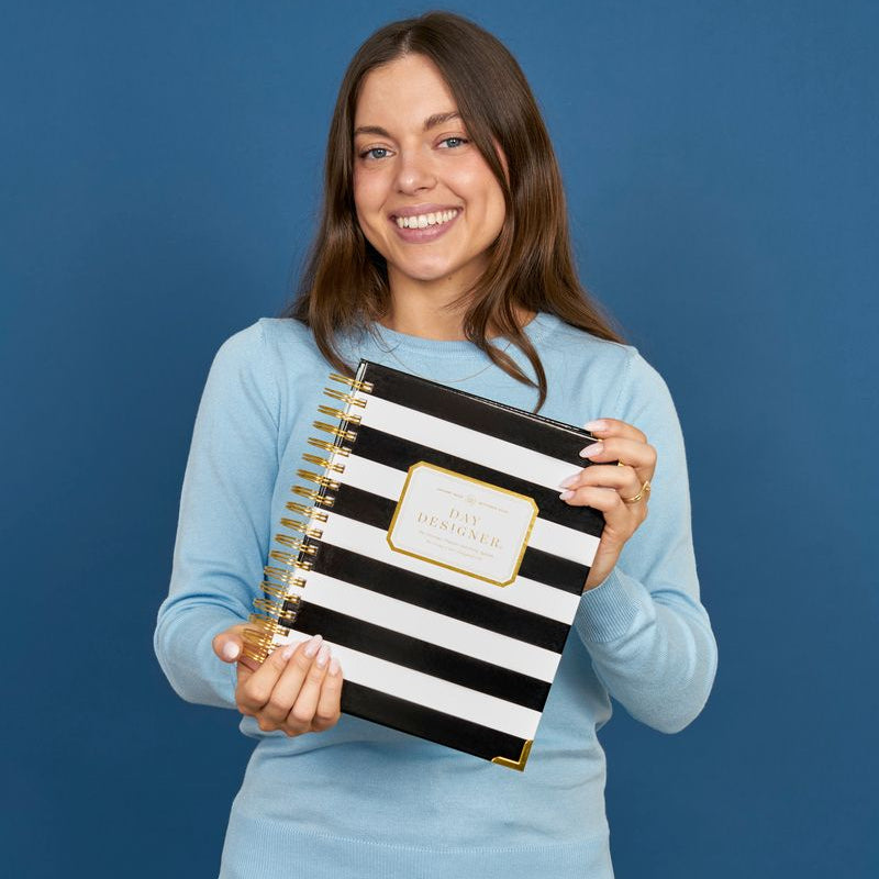 Woman holding a black and white striped notebook against a blue background