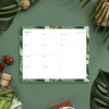 notepad with green and gold tropical leaves on dark green background, bottle, acorns, leaves