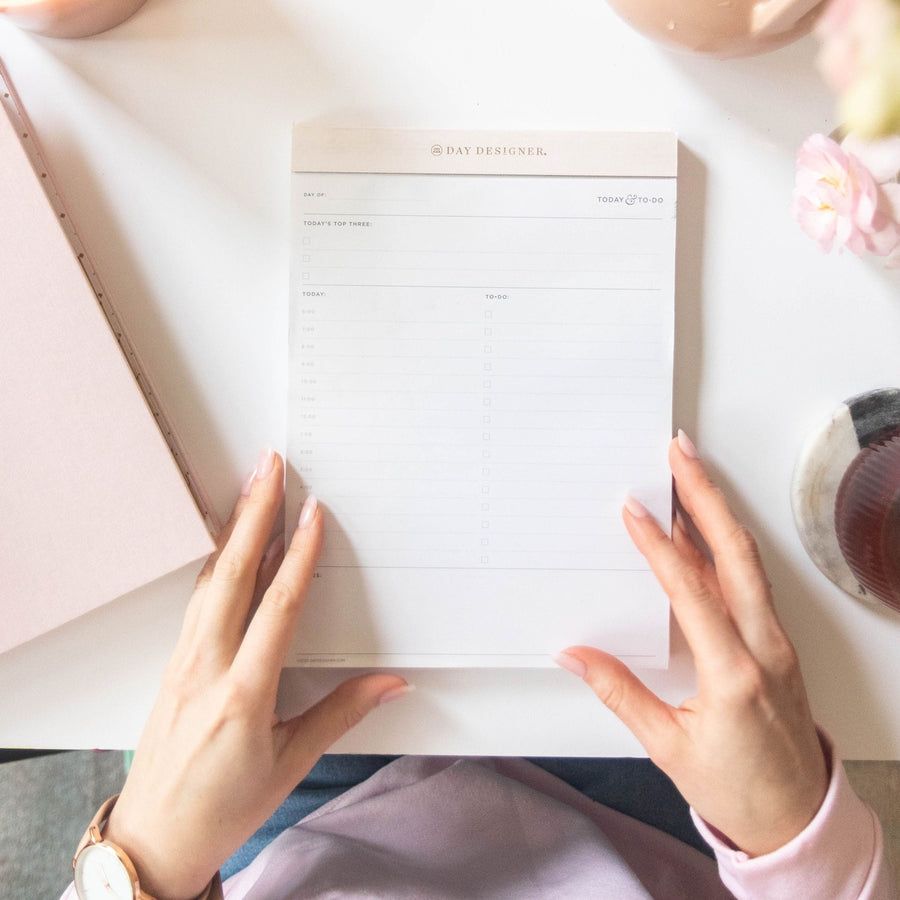 Notepad with blush pink trim on desk with hands, blush planner, tea cup, flower