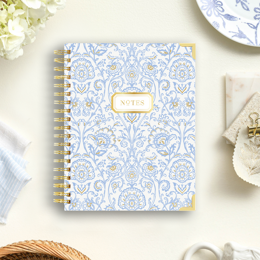 notebook with blue and gold block print pattern, beige background, plate, cloth, flowers, paper clip, basket, antique cup