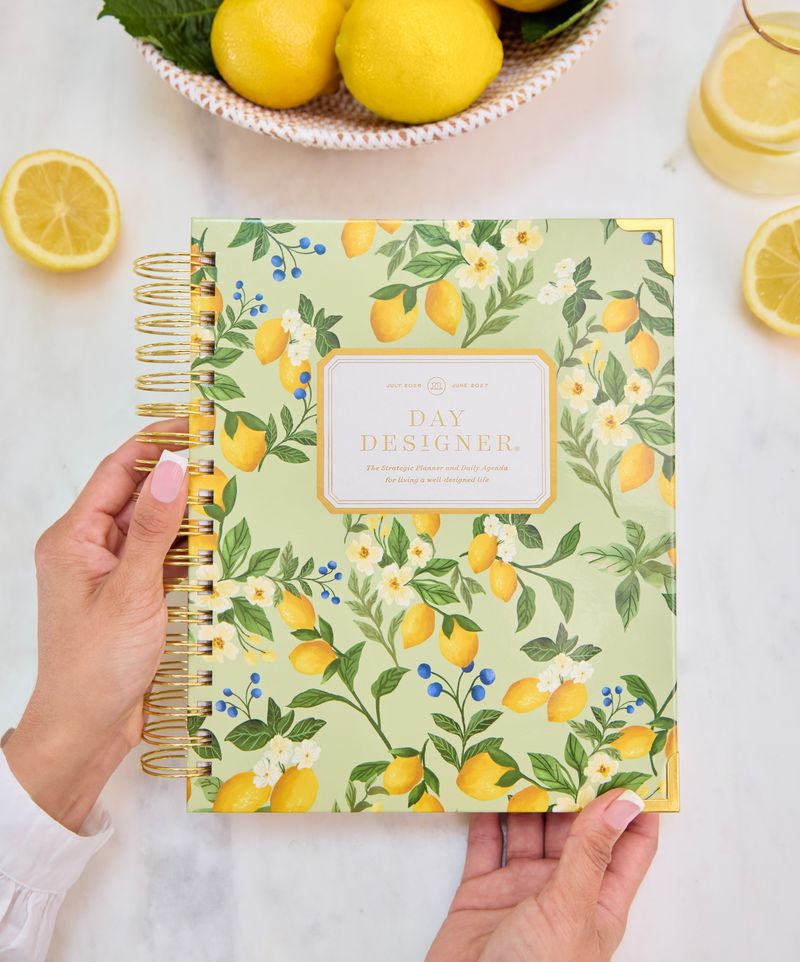 Hand holding a notebook with lemon design, surrounded by lemons on a white surface