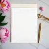 notepad with pink trim on marble background, gold pen and eye glasses, pink peonies