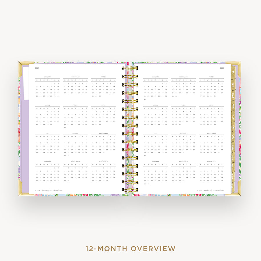 An open 12-month overview planner with a floral patterned cover, gold-toned metal rings, and white interior pages showing a monthly calendar grid, set against a light gray background with the text '12-MONTH OVERVIEW' below.