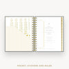 An open spiral-bound planner or pocket organizer shown flat against a light gray background. The pages are white with gold striped accents, gold typography, and a visible Day Designer template on the right page.