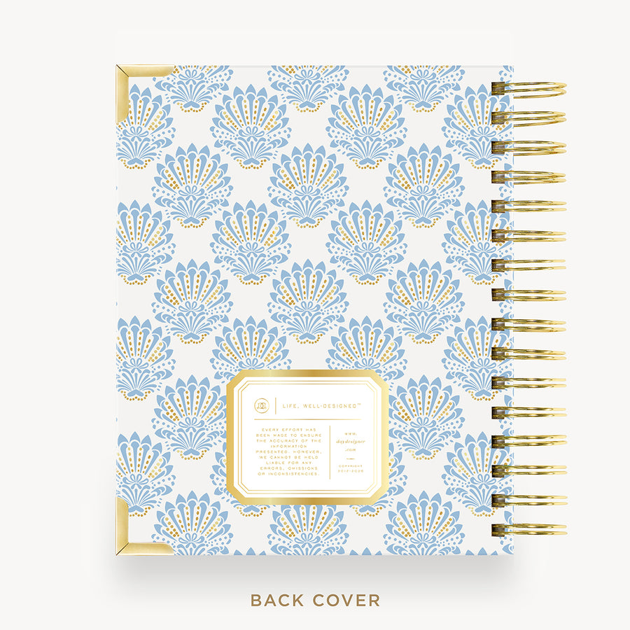 A spiral-bound planner or notebook shown from the back cover, featuring a repeating light blue and gold damask-style pattern on a white background, with gold wire binding and a gold-bordered label area. The text 'BACK COVER' appears below.