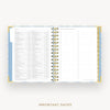 An open spiral-bound planner or agenda on a light gray background, showing a detailed calendar page with columns and a checklist layout. The planner has a light blue and white patterned cover with gold-toned rings and gold page edges.