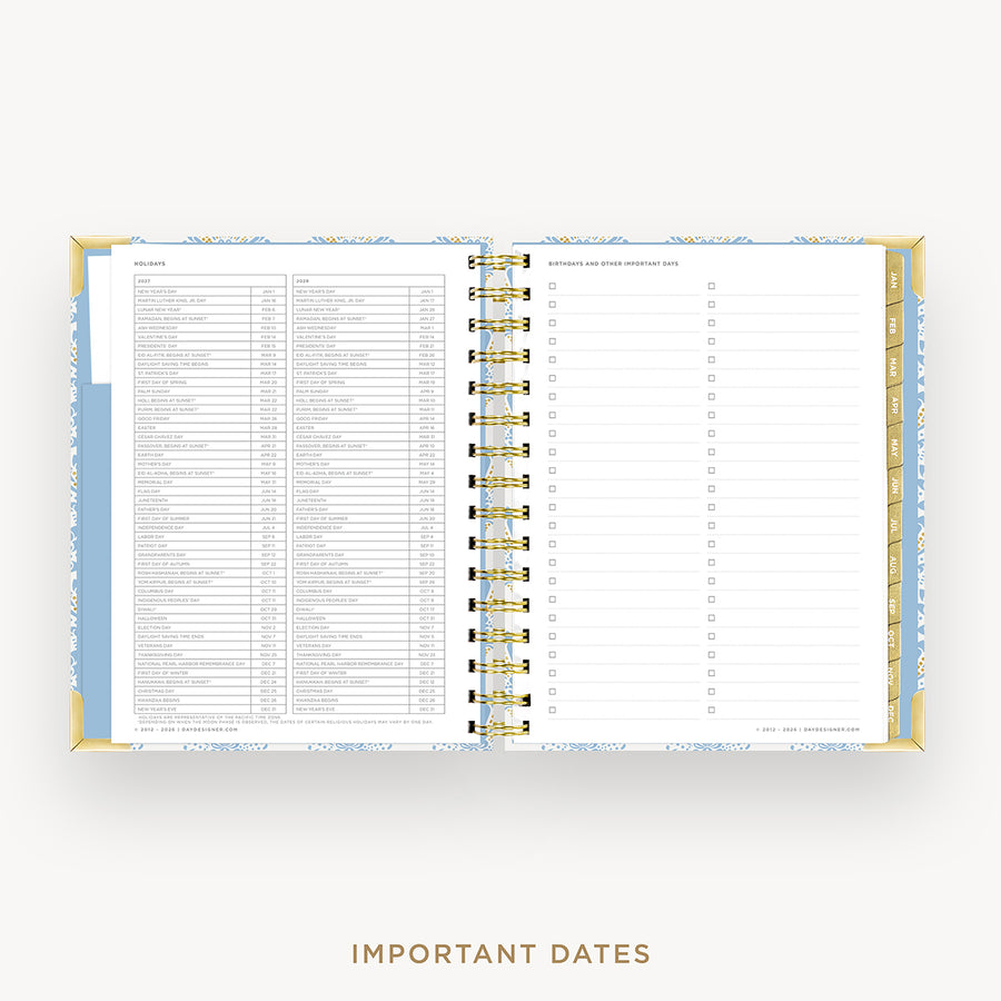 An open spiral-bound planner or agenda on a light gray background, showing a detailed calendar page with columns and a checklist layout. The planner has a light blue and white patterned cover with gold-toned rings and gold page edges.