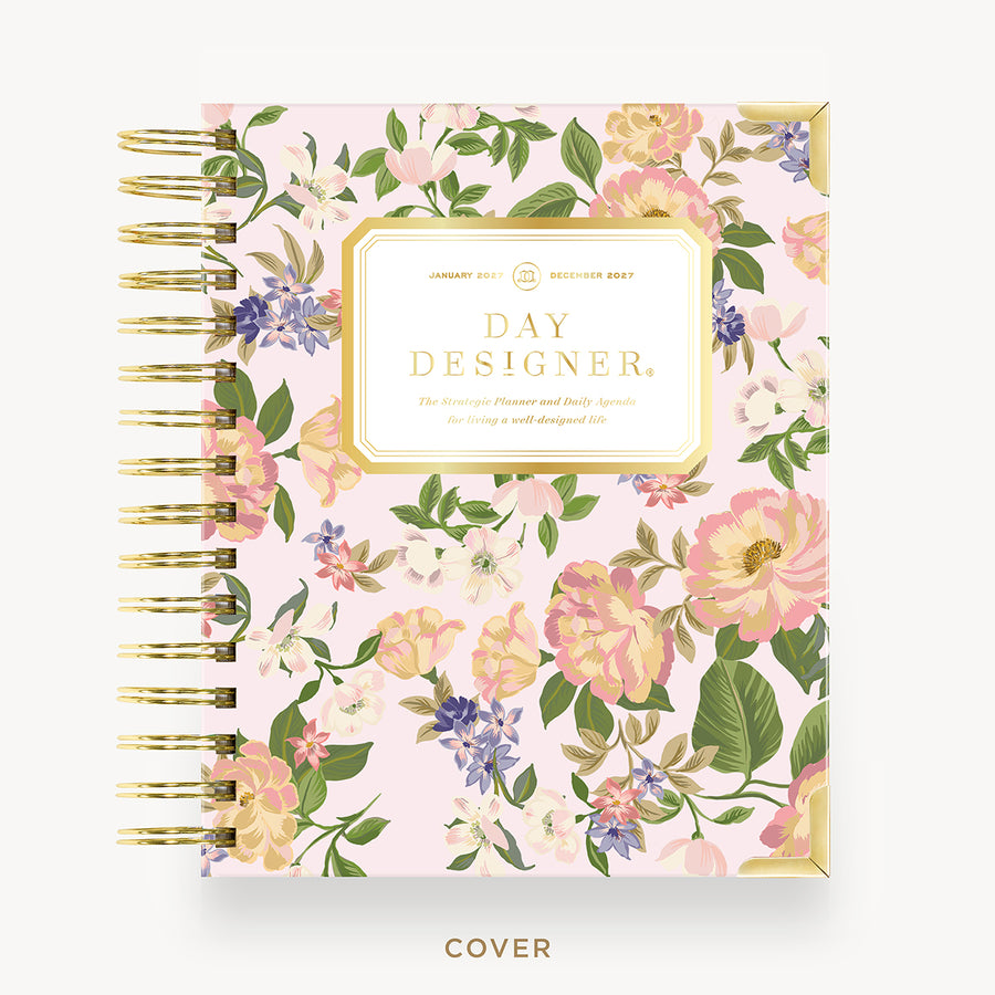A floral spiral-bound planner cover shown from the front on a light gray background. The cover has a pale pink base with an allover watercolor-style floral pattern in pink, peach, cream, green, and small purple blossoms.