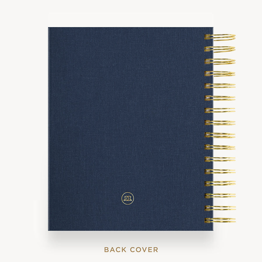 A navy blue textured fabric-bound notebook shown from the back, with gold spiral binding along the right edge and a small circular logo near the bottom. The words 'BACK COVER' appear below on a light gray background.
