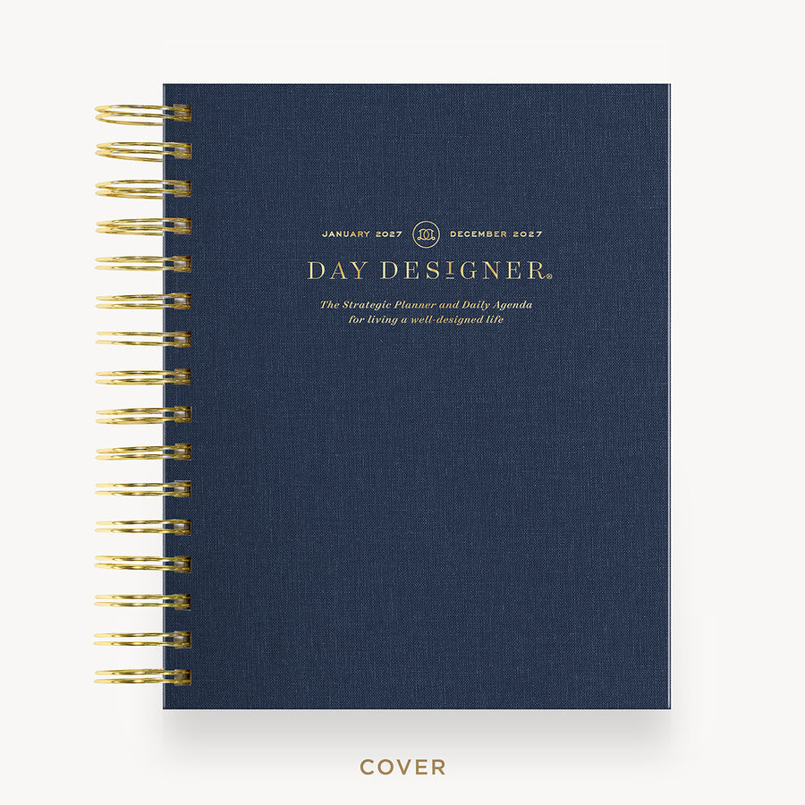 A navy blue textured spiral-bound planner cover with gold foil text reading 'DAY DESIGNER' and gold spiral binding along the left edge, shown on a clean white background with the word 'COVER' below.