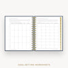 An open spiral-bound planner or workbook showing two printed goal-setting worksheet pages, with gold and black spiral binding and a gold vertical page marker. The pages are centered on a light gray background, with the text 'GOAL-SETTING WORKSHEETS' below.