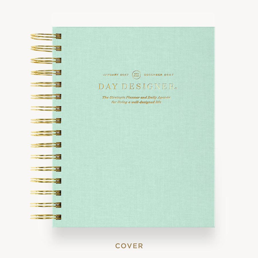 A mint green spiral-bound notebook cover with gold wire binding and gold foil text reading 'DAY DESIGNER' on a clean white background.