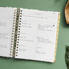 weekly planner, open book, written on pages, gold binding and tabs, green background, palm leaf, brown dish