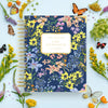 Floral notebook with 'Day Designer' branding surrounded by flowers and butterflies on a light blue background