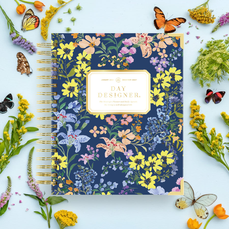 Floral notebook with 'Day Designer' branding surrounded by flowers and butterflies on a light blue background