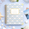 Day Designer notebook with shell pattern on a light blue background with decorative elements.