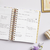 mini weekly planner, open book, written on pages, gold binding and tabs, lilac background, flowers, rolled fabric, frame