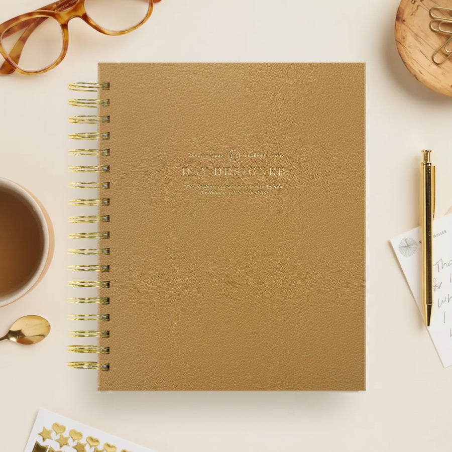 Brown notebook with gold spiral binding on a light surface with stationery items.