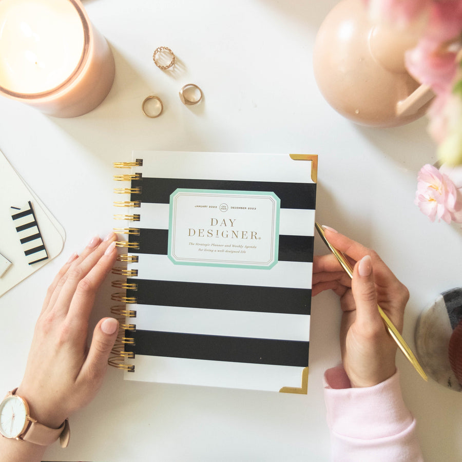 Person holding a black and white striped planner with gold accents on a desk.