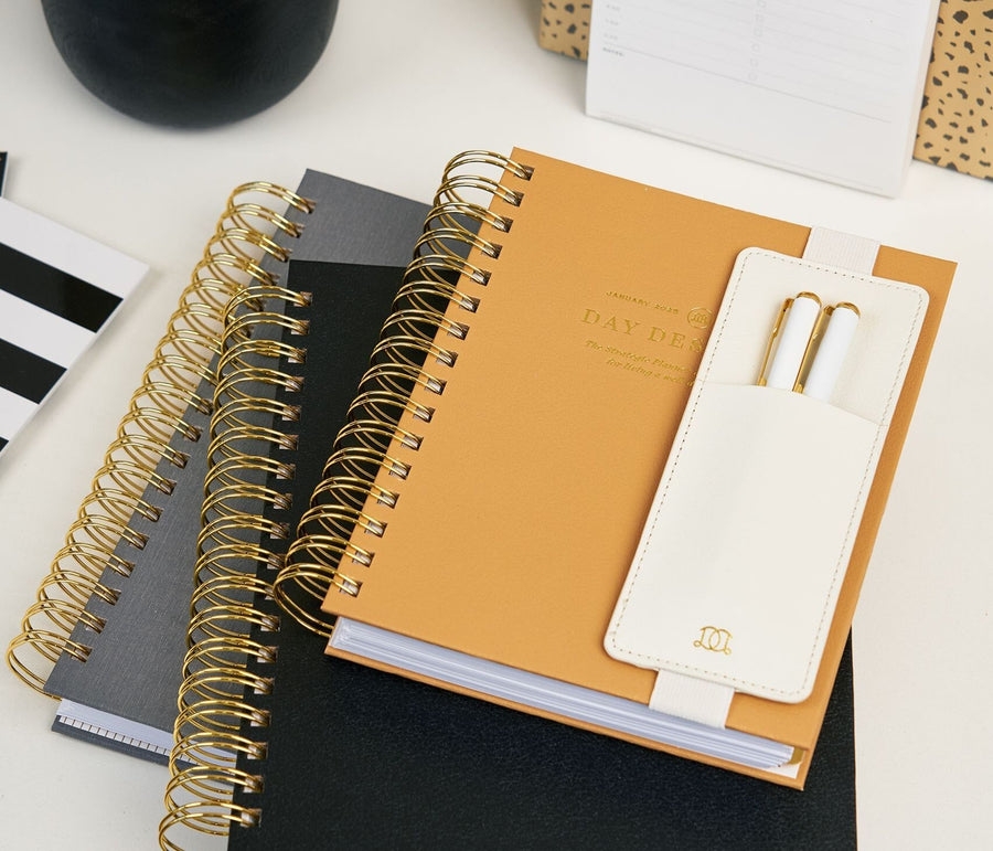 stacked gray, black, and caramel planners, attached pen holder with two pens, notebooks and notepads