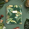 notebook with green and gold tropical leaves on dark green background, bottle, acorns, leaves