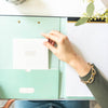 open book clipfolio with notepad, white notes book, hand with gold bracelet, dried flowers, white table