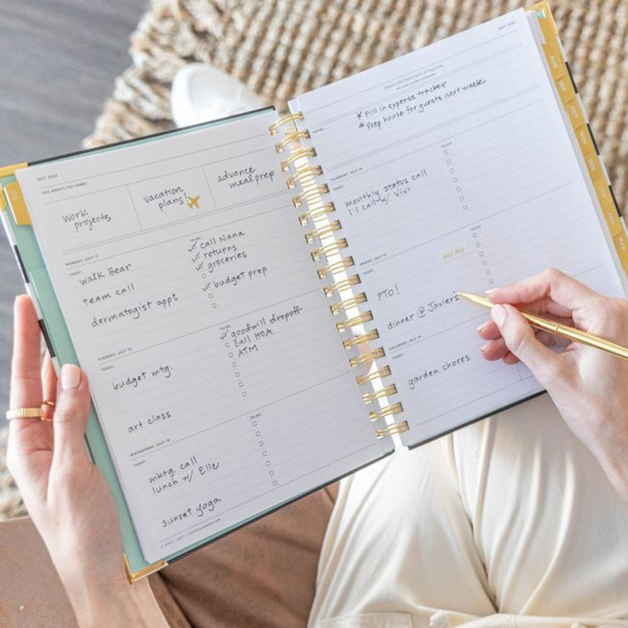 open book planner, written on pages, gold pen, hands, brown rug