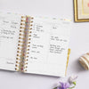 mini daily planner, open book, written on pages, gold binding, purple flowers, picture frame, cloth, lilac background