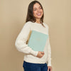 Woman holding a light green planner against a beige background