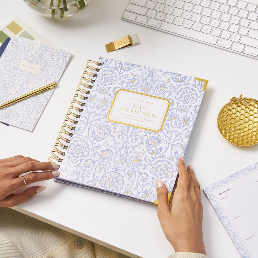 alicia planner, blue and gold block print, gold binding, pen, dish, and pen clip, notebooks, on white desk, keyboard, hands