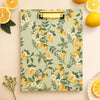 Clipboard with lemon and floral pattern surrounded by lemons on a beige background