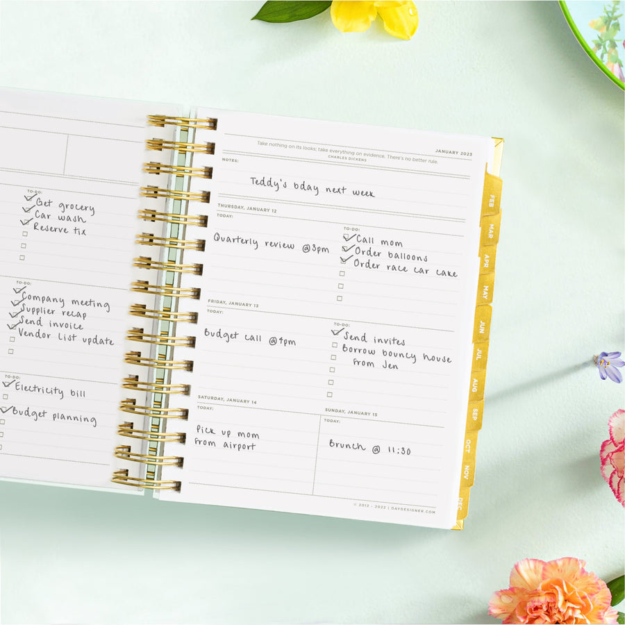mini weekly planner, open book, written on pages, gold binding and tabs, light mint green background, yellow, orange, pink and purple flowers, dish