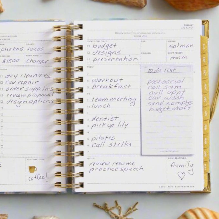 open book planner, written on page, gold binding and monthly tabs, light blue background, shells, gold coral