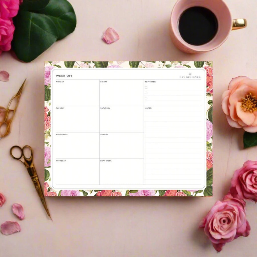 weekly notepad with camellia floral trim, blush background, coffee cup, gold scissors, pink flowers